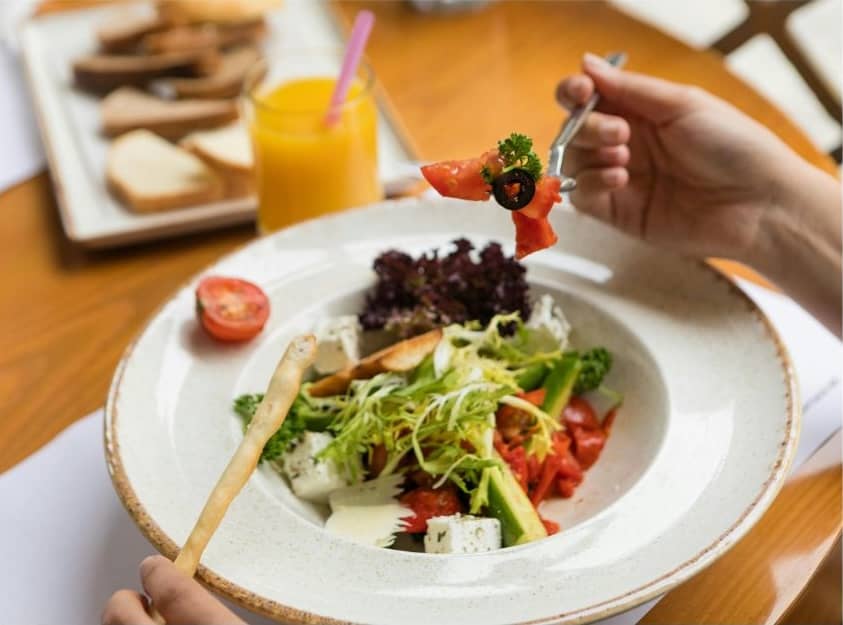 A hand holding a bite of salad on a fork.